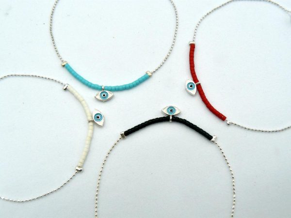 Four Silver-Plated Brass Thin Chain Bracelets With Lobster Clasp Adjustable Closure and Different Bead Colors: One With Black Beads, Another With White Beads, a Third With Turquoise Beads, and the Last One With Red Beads. The Central Piece of Each Bracelet is an Eye of Horus Charm and is Encased in a Layer of Silver Plated Brass
